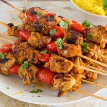 Skewered chicken kebabs on a plate with turmeric rice.