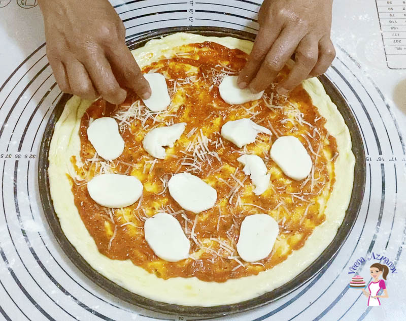 A person adding cheese and toppings to a pizza dough.