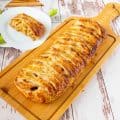 Braided apple puff pastry on a wooden cutting board.
