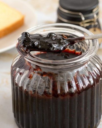 A jar of blueberry jam with a spoon full of jam.