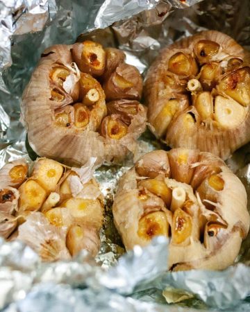Aluminum foil with four heads of roasted garlic.